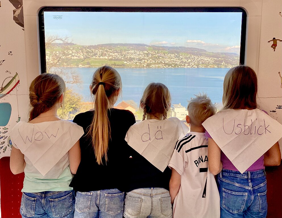 Wettbewerb-Bild: 5 Kinder schauen aus dem Fenster und am Rücken steht: Wow dä Usblick