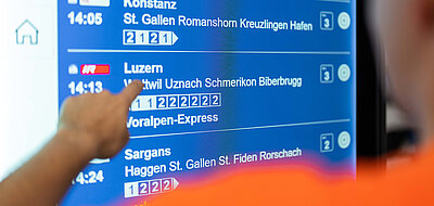 Blick über die Schulter auf das Smart Information Display mit den Abfahrtszeiten der nächsten Züge.