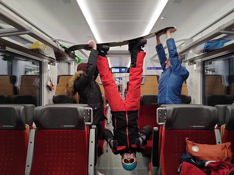 Wettbewerb-Bild: Zwei Personen heben eine Person in die Luft, welche ein Snowboard an hat