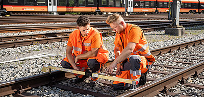 Lernender und Ausbildner sehen sich zusammen eine Arbeit am Gleis an.